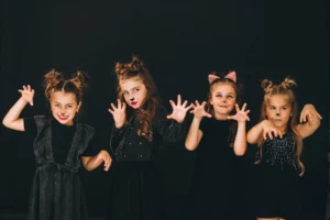 Four girls in cat makeup and costumes posing with claw hands on a black studio background