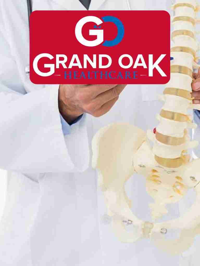 Doctor in white coat holding spine model, Grand Oak Healthcare logo overlay