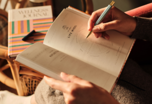 Hands writing in a wellness journal, filling a life wheel diagram with pen in warm light