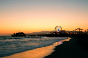 Sunset view of Santa Monica Pier with Ferris wheel lights and ocean waves along the beach