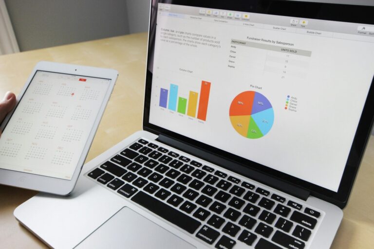 Laptop displays charts and a data table on screen, with a tablet showing a calendar on a desk beside it