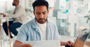 Professional reviewing a report while working on a laptop in a bright modern office workspace