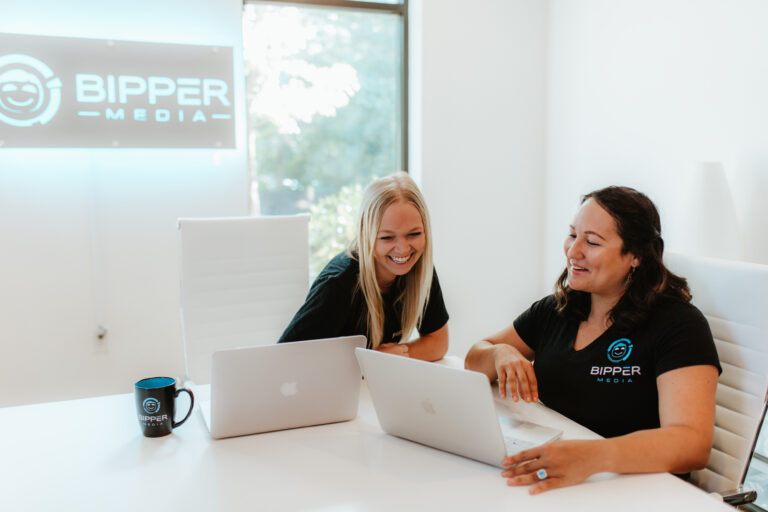 The image showcases a smiling professional working at a desk equipped with various electronic devices, highlighting the collaborative and tech-savvy environment at Bipper Media. This setting reflects the agency's commitment to enhancing client engagement and productivity through innovative digital marketing solutions.