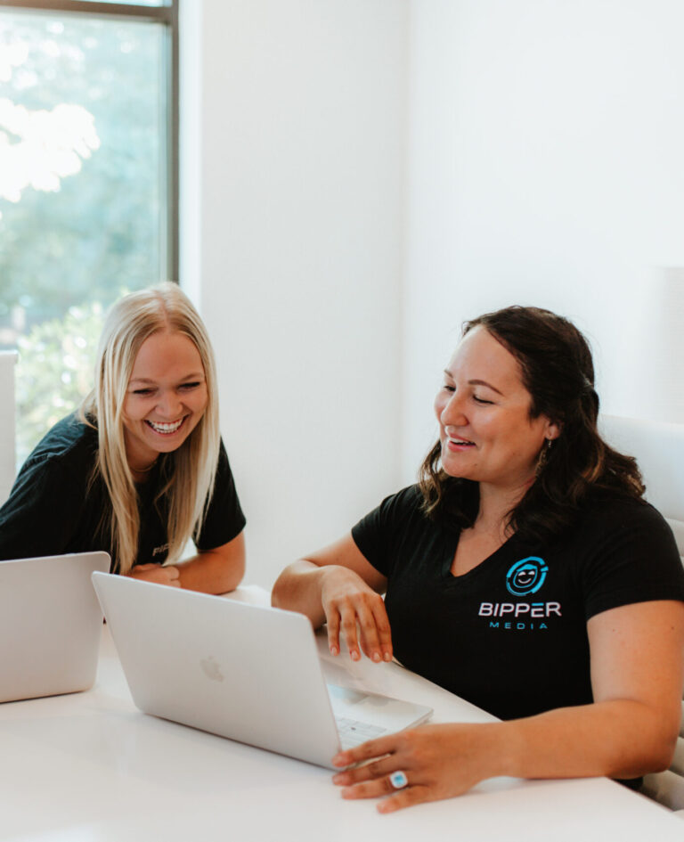 The image showcases a smiling professional working at a desk equipped with various electronic devices, highlighting the collaborative and tech-savvy environment at Bipper Media. This setting reflects the agency's commitment to enhancing client engagement and productivity through innovative digital marketing solutions.